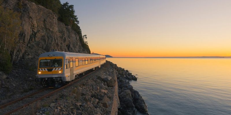 Le train de Charlevoix longeant une montagne avec une vue sur couché du soleil.