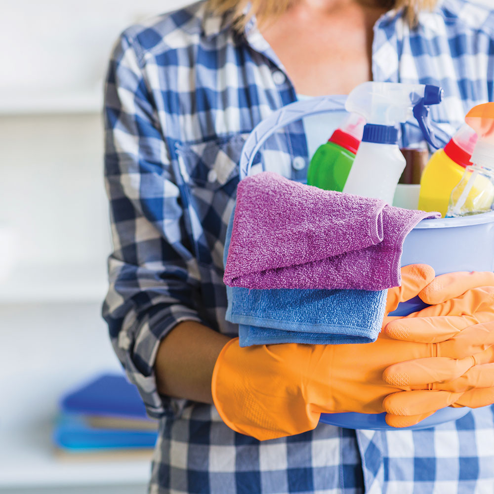 Femme tenant un seau contenant des produits nettoyants.